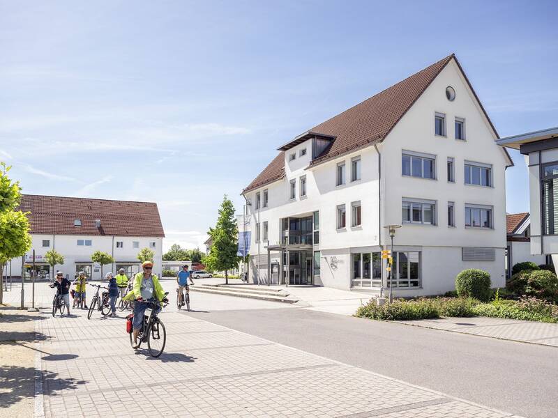Rathausplatz Burgrieden mit Rathaus im Hintergrund und einer Gruppe Fahrradfahrer